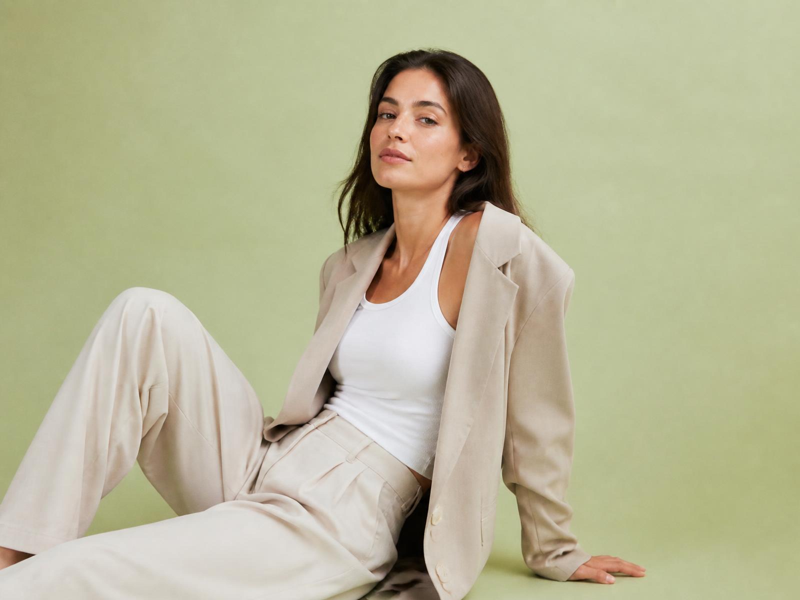 Confident woman in a white tank and oversized beige blazer against a pale green studio backdrop